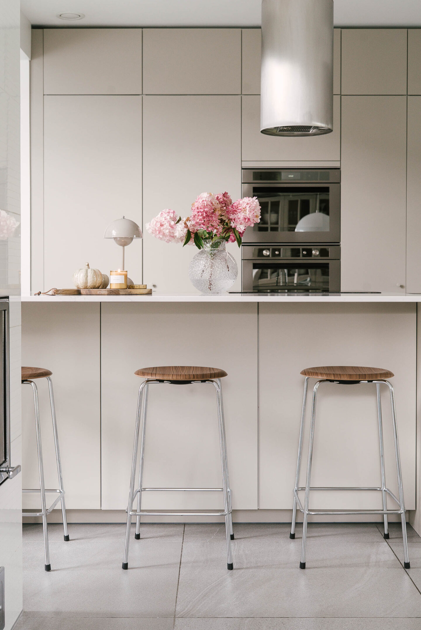 Moderni ja minimalistinen beige keittiö, jossa Fritz Hansenin Dot-baarijakkarat saarekkeen ääressä